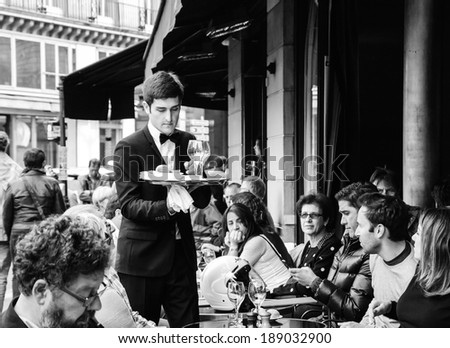 PARIS, FRANCE - APRIL 20, 2014 : Waiter serving customers at traditional outdoor Parisian cafe in center city.