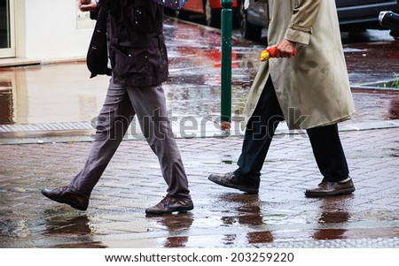Legs in leather shoes in motion (of two men - senior and young) on the wet street. Colorful reflection on brown pavement.