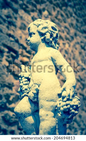 Statue of Bacchus (Dionysus) with grapes in his hands against rough stone wall. Garden sculpture. (Chateauneuf du Pape, Provence, France) Aged photo.
