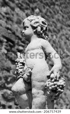 Statue of Bacchus (Dionysus) with grapes in his hands against rough stone wall. Garden sculpture. (Chateauneuf du Pape, Provence, France) Aged photo. Black and white.