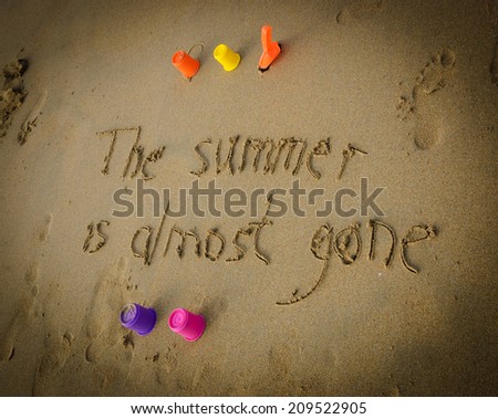A sentence written on the sand of a beach: THE SUMMER IS ALMOST GONE,  four colorful molds and shovel . Vacation end / back from holiday / back to the work or school concept. Vignette effect.