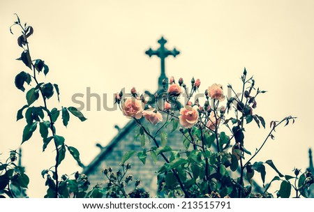 Cross and roses. A church in Dinan (Brittany, France). Selective focus on the flowers. Retro aged photo.