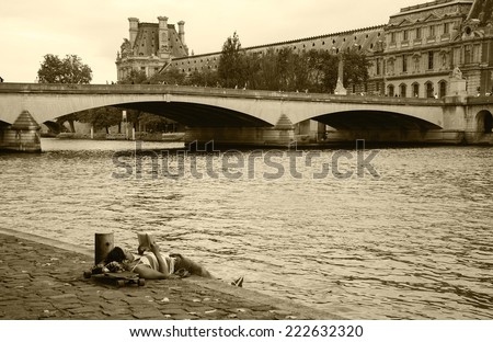 PARIS, FRANCE - OCTOBER 4, 2014: Unidentified young man laying on his skateboard and reading on Seine bank near Louvre museum. Seine embankment is very popular promenade at weekends.