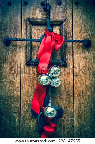 Christmas decoration on the wooden door. Red ribbon and four silver balls with street reflection. Aged photo.