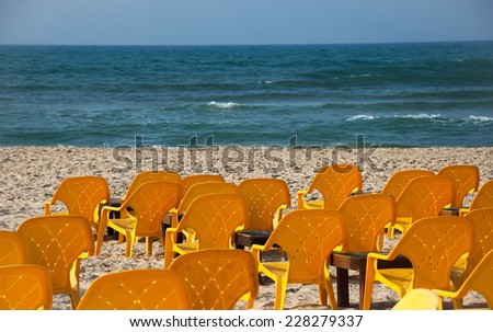 Empty yellow chairs and wooden tables on the sandy beach (Tel Aviv, Israel) Selective focus on the first row of chairs and the sand.