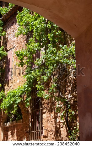 An old house overgrown with grape vine. A view through the street arch. Roussillon ocher village (included in the list of \
