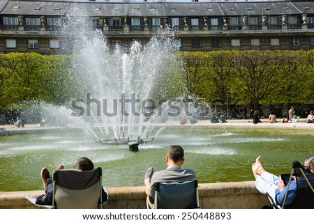 PARIS, FRANCE - APRIL 21, 2013: People relaxing around a fountain in Palais Royal garden. Palais-Royal houses the Council of State, the Constitutional Council, and the Ministry of Culture of France.