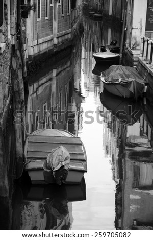 Narrow canal in Venice. Boats and reflection of houses in the water. Selective focus on the reflection. Aged photo. Black and white.