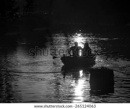 Silhouettes of  a man and woman in the boat on the lake. Sunset. Light and shadow. Romance background. Harmony with nature idea. Aged photo. Black and white.