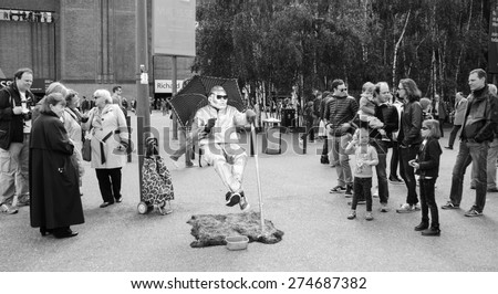 LONDON, ENGLAND, UK - MAY 3, 2014: Unidentified floating man in silver costume sitting in the air near Tate gallery. Most of London street artists perform in tourist hot spots.