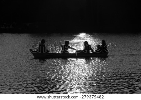 Family in the boat on the lake in sunset glow. Silhouettes. Harmony with nature idea.  Aged photo. Black and white.