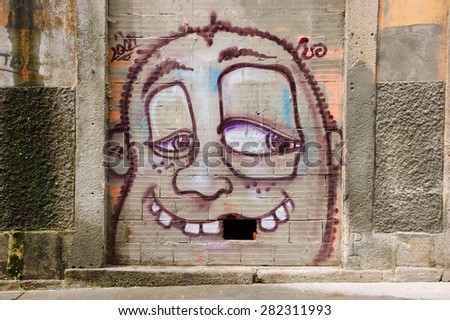 PORTO, PORTUGAL - APRIL 26, 2015: Funny face with mussing tooth (missing brick in the wall).  Graffiti artist Costah uses a particular features of locations to create his cartoon style images.