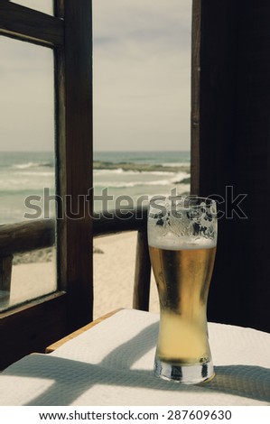 Cold beer on cafe terrace with the view on the ocean beach through the opened window. Algarve, Portugal. A game of light an shadow. Aged toned photo.