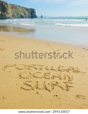 Words PORTUGAL, OCEAN and SURF are written on the scenic beach in the Algarve region of Portugal. People swimming and surfing.