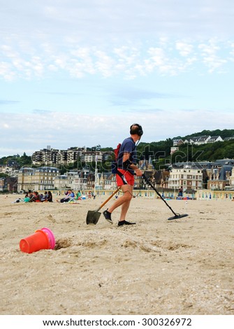 TROUVILLE-SUR-MER, FRANCE - JULY 10, 2015: Man searching for the treasure (jewelry, coins and other valuable metal items that were lost in the beach\'s sand during the day) using a metal detector.
