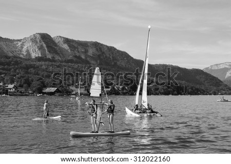 ANNECY LAKE, FRANCE - AUGUST 27, 2015: Tourists enjoy from water sports (sailing, kayaking) at Annecy lake surrounded by beautiful mountains. Annecy Lake is one of the most popular French resorts.