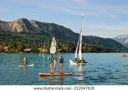ANNECY LAKE, FRANCE - AUGUST 27, 2015: Tourists enjoy water sports (sailing, kayaking) at Annecy lake surrounded by beautiful mountains. Annecy Lake is one of the most popular French resorts.