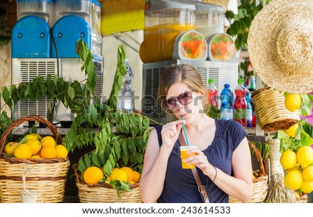 Pretty young girl drinks fresh orange juice through a straw at a street stall in Sicily