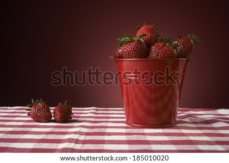 fresh red strawberries in a red bowl on checkered tablecloth, with red background