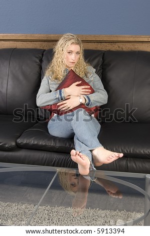 Beautiful blond, sitting on black leather couch holding red pillow