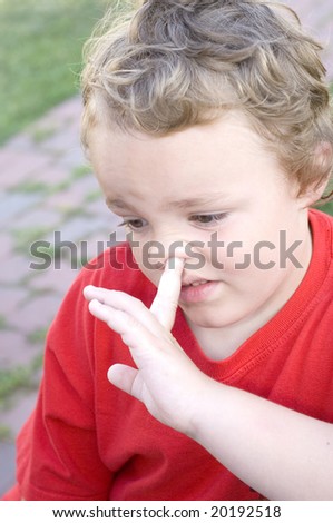 Young blond boy picking nose with index finger