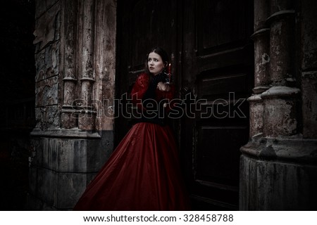Mysterious woman in red Victorian dress with a candle