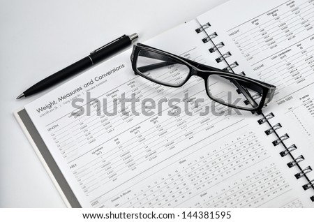 glasses and black pen on weight , measures and conversion book