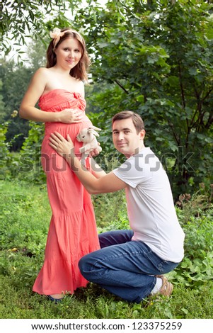 man and his pregnant wife have fun in the park rlaying with rabbit toy