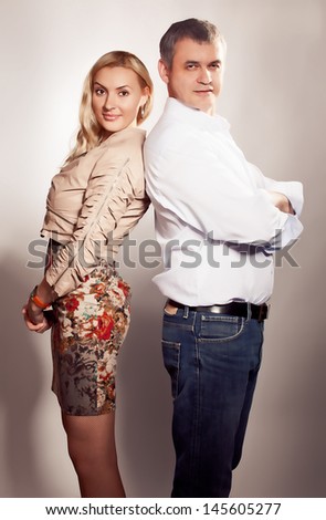 couple standing together, posing in studio, looking at camera. Man is older woman