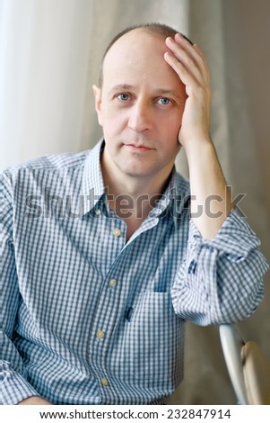 Portrait of smart bald man wearing a striped shirt sitting near the window