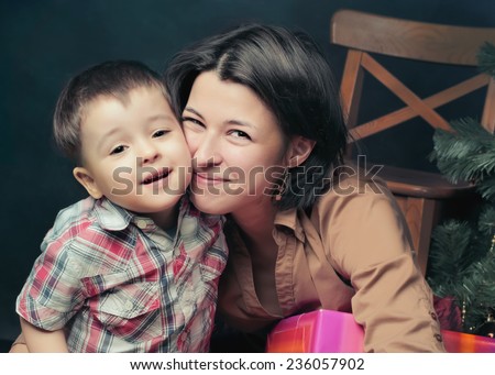 Mother ans boy near Christmas tree with gifts. Son kissing mommy