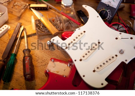 Red electric guitar on guitar repair desk or in a  repair work shop. Neck and pickguard detached. Double cutaway solid body guitar, red metallic color. Shallow depth of field.