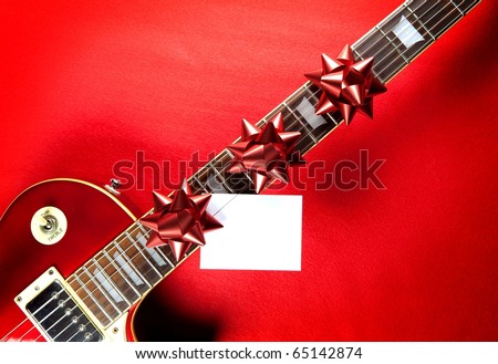 Red guitar with red ribbon bows and white blank card on neck fret board. Concept image for invitation to a holiday musical event or, a  christmas present electric guitar.