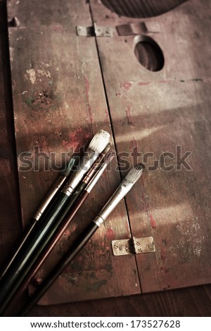 Old painting brushes and a wooden palette on an old painters desk.