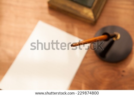 Retro style pen, pen stand and paper or memo on wooden desk. Focus is on pen tip.