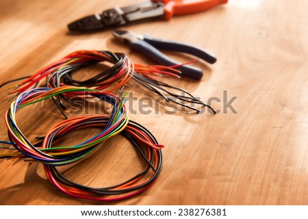 Colored cables or wires and a wire cutter tools on a wooden work desk, with by-the-window type lighting environment.