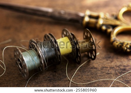 Vintage sewing machine bobbins with vintage gold ( brass ) scissors on a old grungy work table. Tailor\'s work table. textile or fine cloth making. Shallow depth of field.