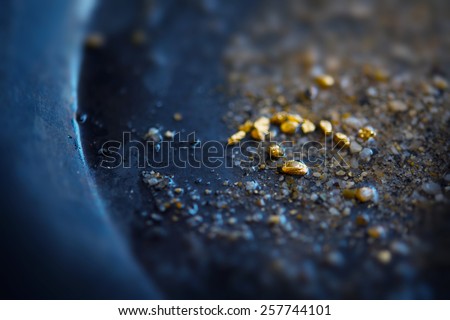 Gold dIscovery. Gold on grungy wash pan with river sand. Gold panning or digging. Very shallow depth of field due to subject size.