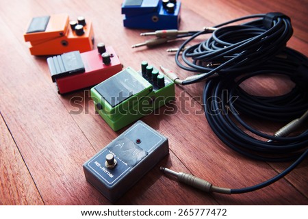 Setting up guitar audio processing effects. Electric guitar stomp box effectors and cables on studio floor. Focus is on forehand switch box. Intentionally shot with impressional feel and tone.