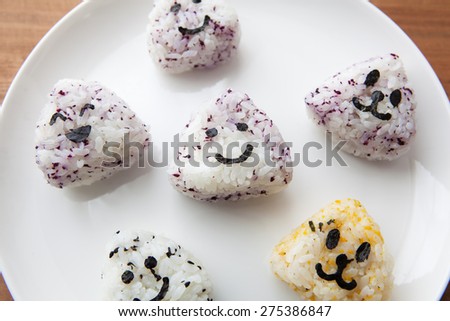 Onigiri rice balls with smiley faces made with cut out nori seaweed, on white plate.