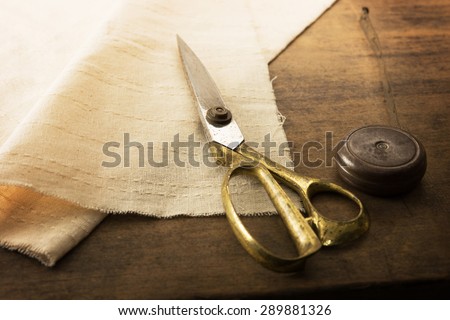 Gold scissors and natural white fabric. Measuring, cutting, sewing textile or fine cloth. Work table of a tailor. Shallow depth of field, Focus on scissors