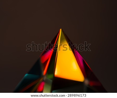 Refractions of light in a glass prism. Shallow depth of field. Focus is on the area little beneath the tip.