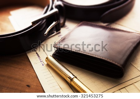 Documents, pen, belt and a leather wallet on a wooden desk. hotel table or gentleman\'s desk. shallow depth of field.