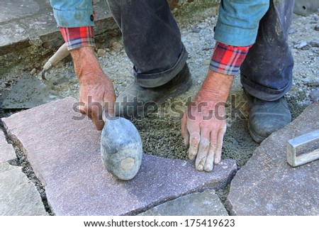 senior landscape gardener fitting a flagstone tile with a rubber mallet..