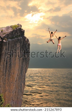 two girls jumping from cliff rock, coastal landscape in the evening