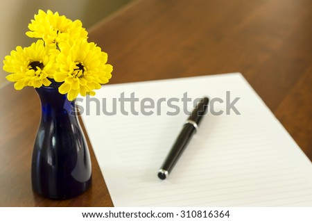 Blank letter and a pen with Yellow Chrysanthemum in the blue vase on the table