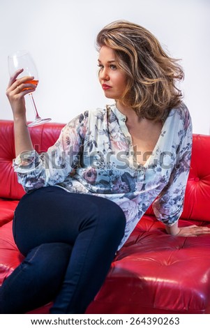 Young lady holding glass of red wine and sitting on sofa.