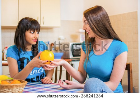 Two women having conversation and one of them giving or showing a orange to her friend.