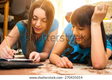 Two happy young female students preparing for exam while lying on floor in the room.