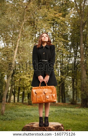 full length portrait of young female standing on stump in forest with bag looking away